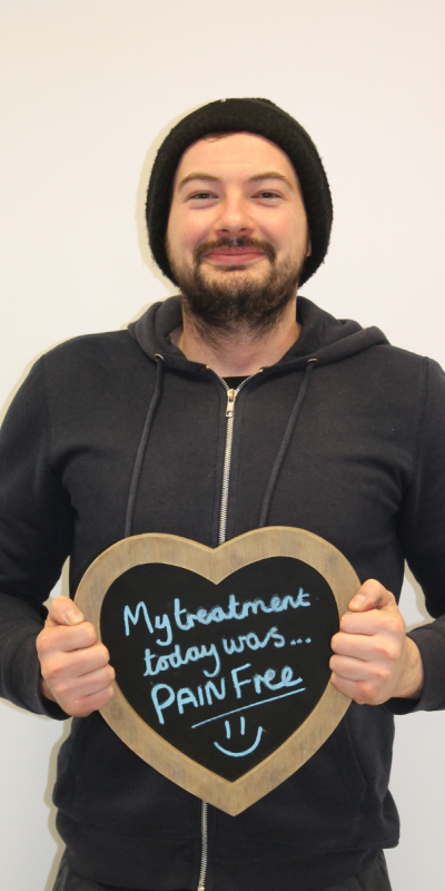 Patient at Hampshire Dentists, holding a sign saying " My treatment today was pain free " emphasising pain-free dental care.
