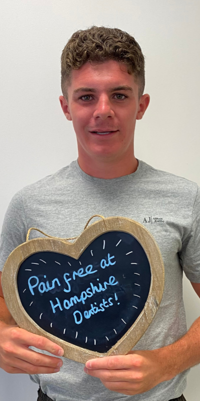 Patient at Hampshire Dentists, holding a sign saying "Pain free at Hampshire Dentists" emphasising pain-free dental care.