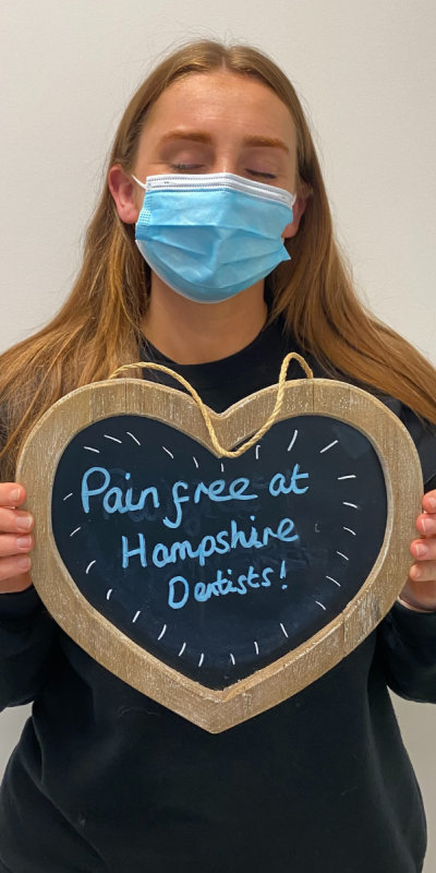 Patient at Hampshire Dentists, holding a sign saying "Pain free at Hampshire Dentists" emphasising pain-free dental care.