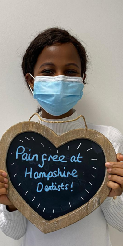 Patient at Hampshire Dentists, holding a sign saying "Pain free at Hampshire Dentists" emphasising pain-free dental care.