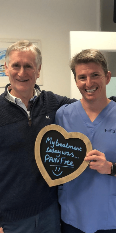 Patient Photos - Hampshire Dentists Pain Free Dentist in Southampton Patient with Dr Robin Hanna at Hampshire Dentists, holding a sign saying "My treatment today was pain free" emphasising pain-free dental care.