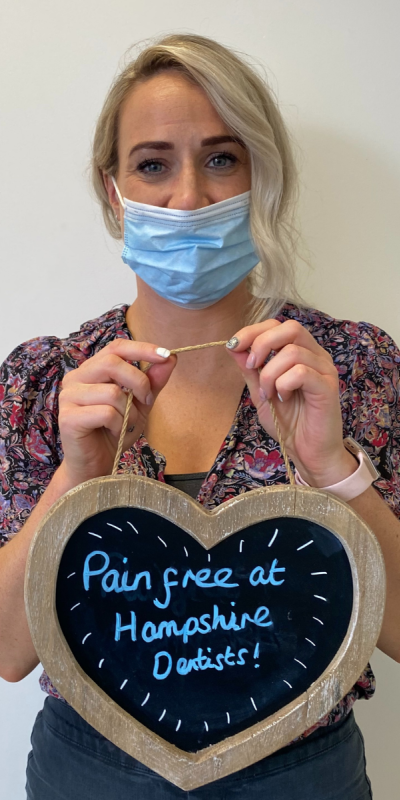 Patient at Hampshire Dentists, holding a sign saying "Pain free at Hampshire Dentists" emphasising pain-free dental care.
