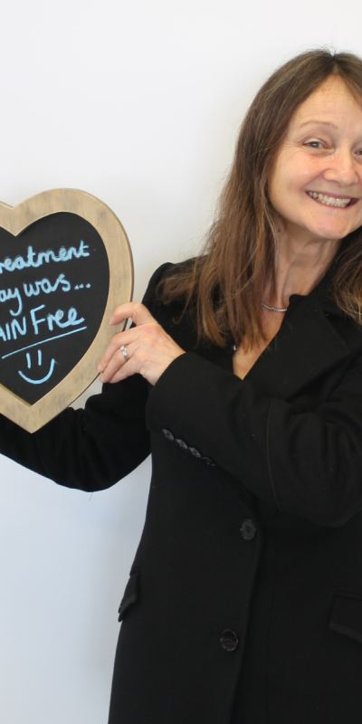 Patient at Hampshire Dentists, holding a sign saying " My treatment today was pain free " emphasising pain-free dental care.