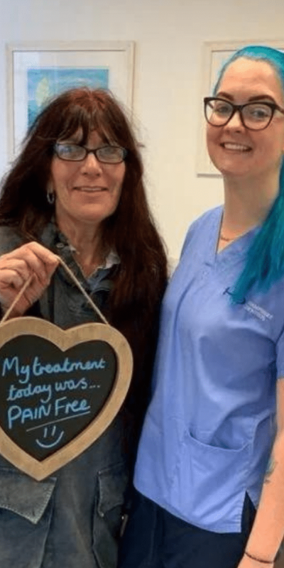 Patient Photos - Hampshire Dentists Pain Free Dentist in Southampton Patient with Dental nurse at Hampshire Dentists, holding a sign saying "My treatment today was pain free" emphasising pain-free dental care.
