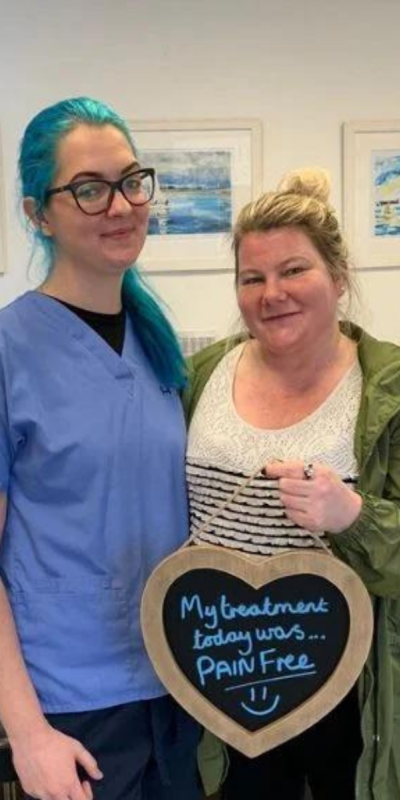 Patient with Dental nurse at Hampshire Dentists, holding a sign saying "My treatment today was pain free" emphasising pain-free dental care.