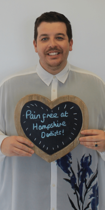 Patient Photos - Hampshire Dentists Pain Free Dentist in Southampton Patient at Hampshire Dentists, holding a sign saying "Pain free at Hampshire Dentists" emphasising pain-free dental care.