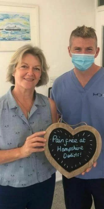Patient with Dr Robin Hanna at Hampshire Dentists, holding a sign saying " Pain free at Hampshire Dentists" emphasising pain-free dental care.