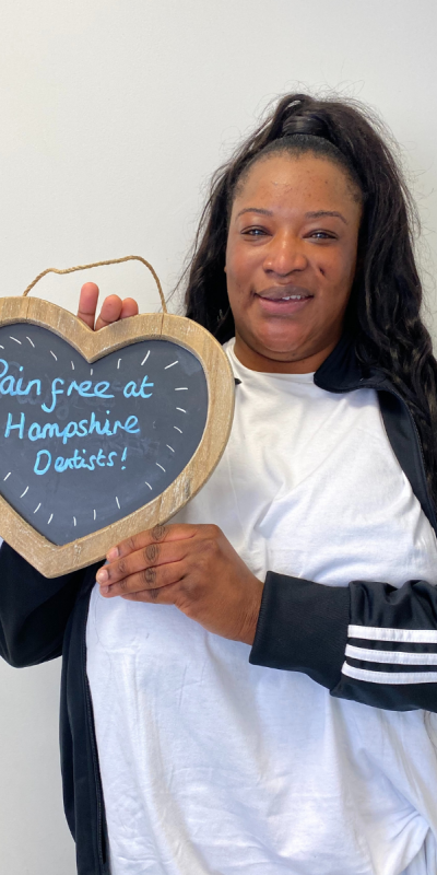 Patient at Hampshire Dentists, holding a sign saying "Pain free at Hampshire Dentists" emphasising pain-free dental care.