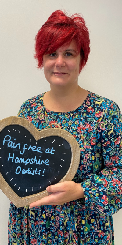 Patient at Hampshire Dentists, holding a sign saying "Pain free at Hampshire Dentists" emphasising pain-free dental care.