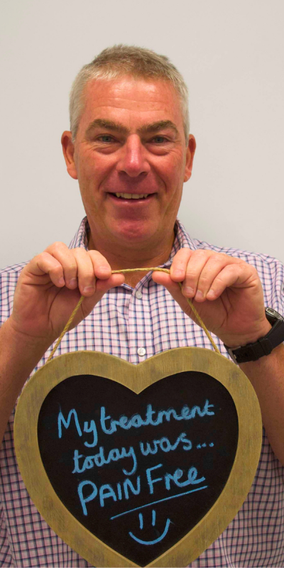 Patient at Hampshire Dentists, holding a sign saying " My treatment today was pain free " emphasising pain-free dental care.