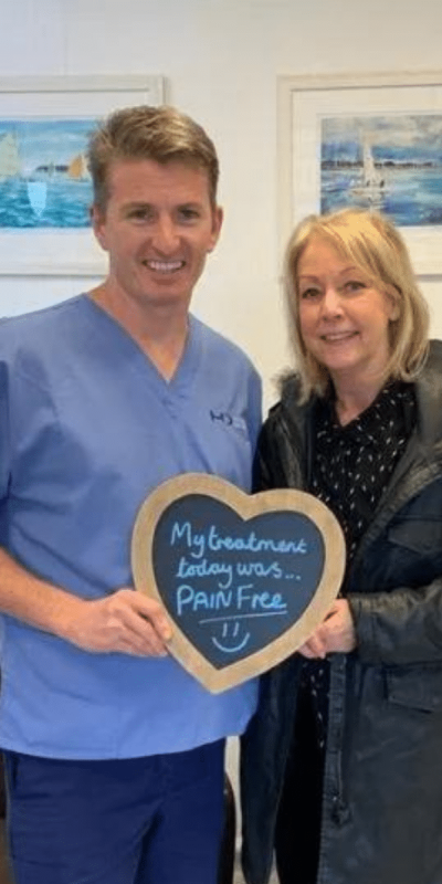 Patient Photos - Hampshire Dentists Pain Free Dentist in Southampton Patient with Dr Robin Hanna at Hampshire Dentists, holding a sign saying "My treatment today was pain free" emphasising pain-free dental care.
