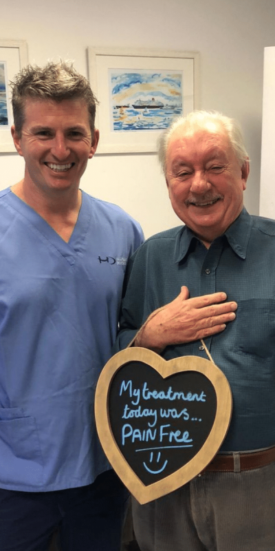Patient Photos - Hampshire Dentists Pain Free Dentist in Southampton Patient with Dr Robin Hanna at Hampshire Dentists, holding a sign saying "My treatment today was pain free" emphasising pain-free dental care.