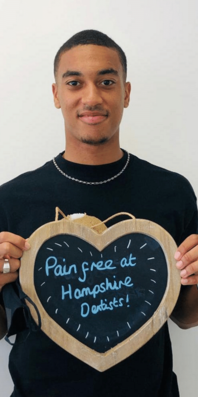 Patient Photos - Hampshire Dentists Pain Free Dentist in Southampton Patient at Hampshire Dentists, holding a sign saying "Pain free at Hampshire Dentists" emphasising pain-free dental care.
