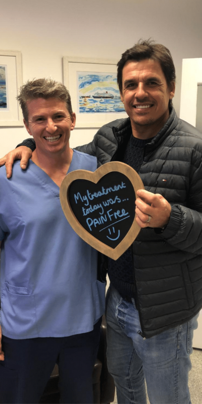 Patient Photos - Hampshire Dentists Pain Free Dentist in Southampton Patient with Dr Robin Hanna at Hampshire Dentists, holding a sign saying "My treatment today was pain free" emphasising pain-free dental care.