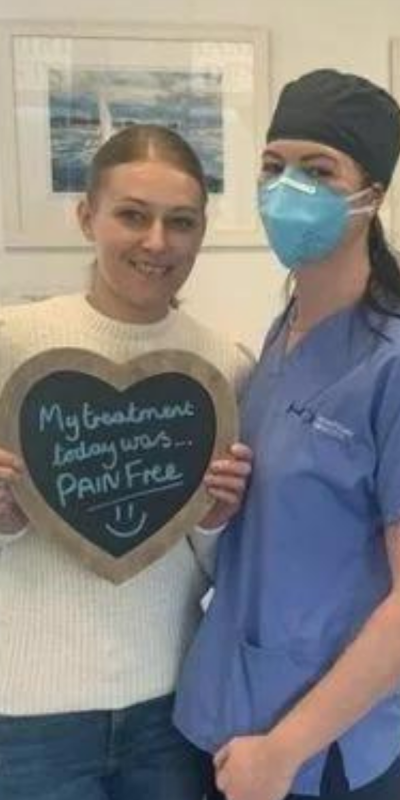 Patient with Dental nurse at Hampshire Dentists, holding a sign saying "My treatment today was pain free" emphasising pain-free dental care.