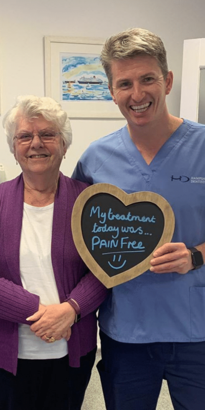 Patient Photos - Hampshire Dentists Pain Free Dentist in Southampton Patient with Dr Robin Hanna at Hampshire Dentists, holding a sign saying "My treatment today was pain free" emphasising pain-free dental care.