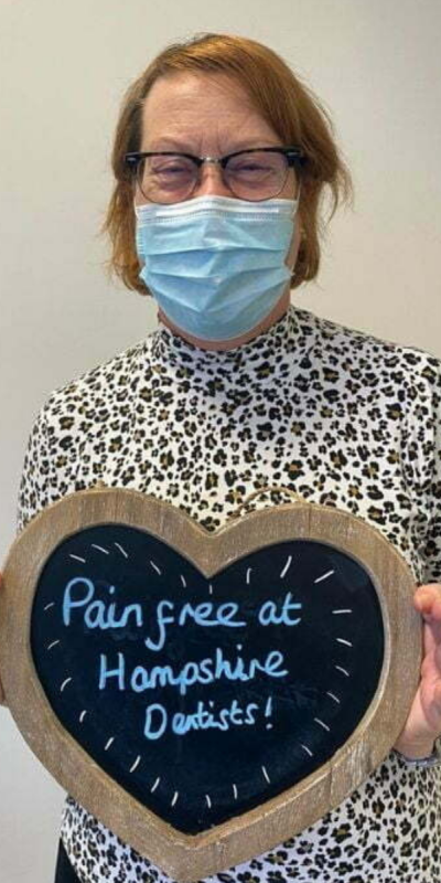 Patient at Hampshire Dentists, holding a sign saying "Pain free at Hampshire Dentists" emphasising pain-free dental care.