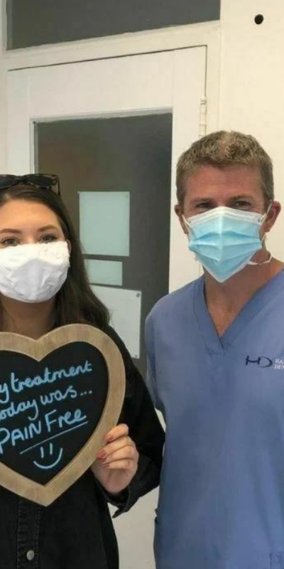 Patient with Dr Robin Hanna at Hampshire Dentists, holding a sign saying "My treatment today was pain free" emphasising pain-free dental care.