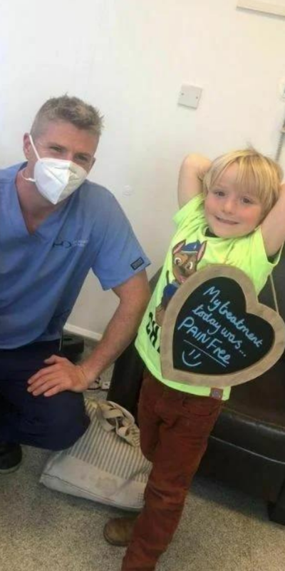 Patient with Dr Robin Hanna at Hampshire Dentists, holding a sign saying "My treatment today was pain free" emphasising pain-free dental care.