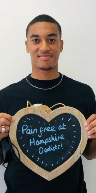 Patient at Hampshire Dentists, holding a sign saying "Pain free at Hampshire Dentists" emphasising pain-free dental care.