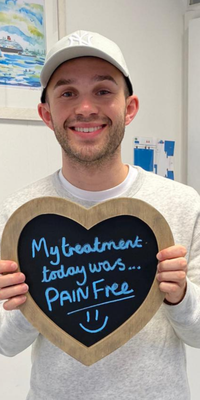 Patient at Hampshire Dentists, holding a sign saying " My treatment today was pain free " emphasising pain-free dental care.