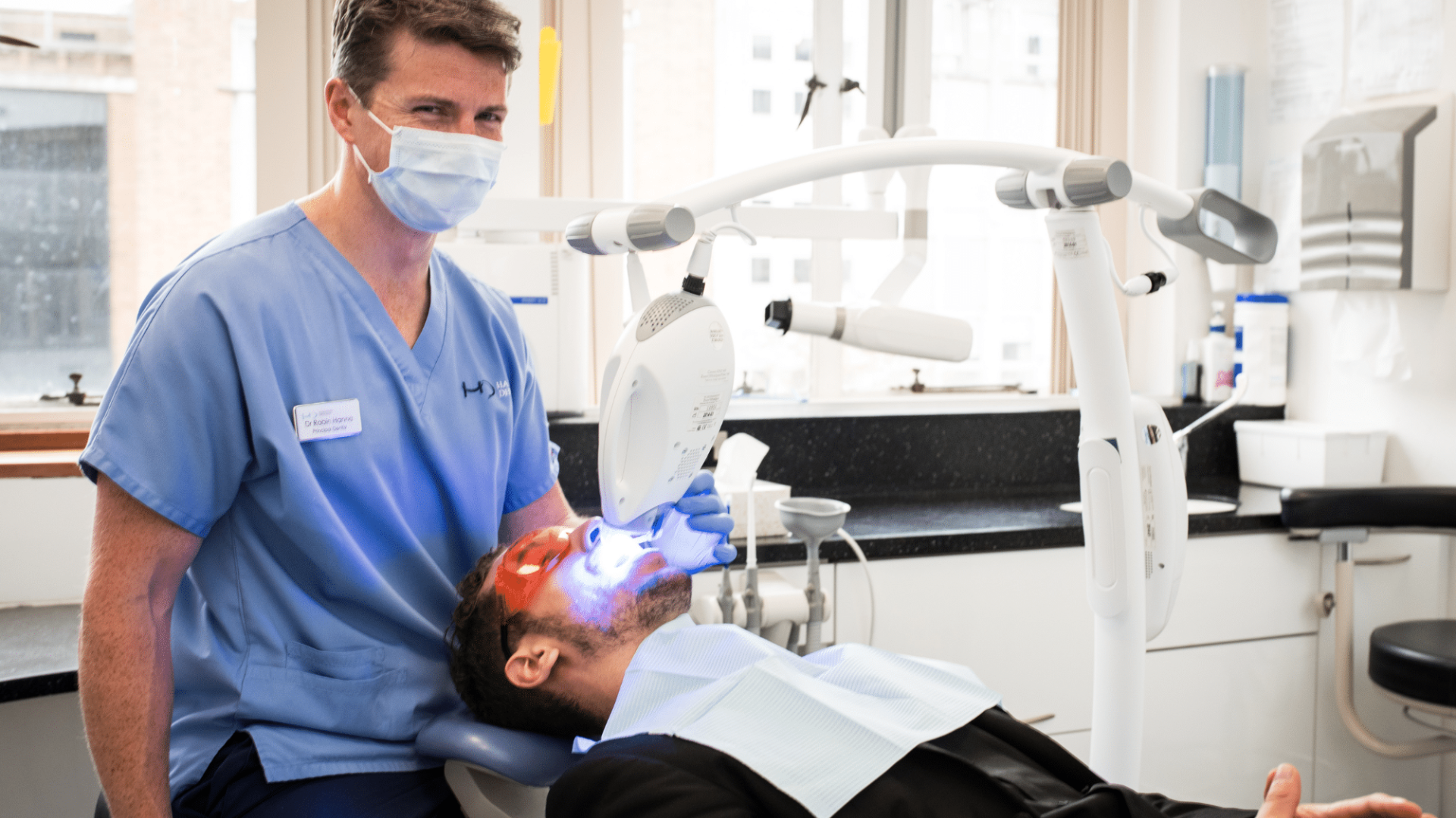 Dr Robin Hanna, Implantologist - Hampshire Dentists Pain Free Dentist in Southampton Dr Robin Hanna completing light activated power teeth whitening treatment on patient lying back in the dental chair