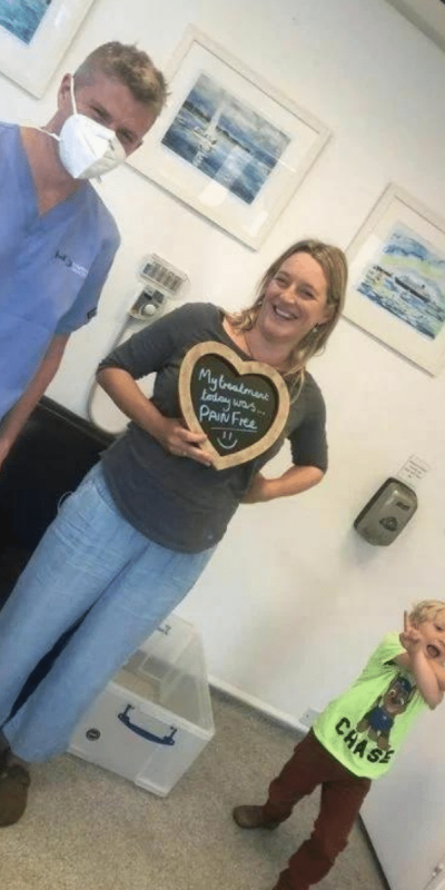 Patient Photos - Hampshire Dentists Pain Free Dentist in Southampton Patient with Dr Robin Hanna at Hampshire Dentists, holding a sign saying "My treatment today was pain free" emphasising pain-free dental care.