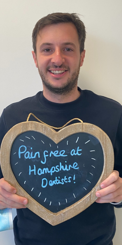 Patient at Hampshire Dentists, holding a sign saying "Pain free at Hampshire Dentists" emphasising pain-free dental care.