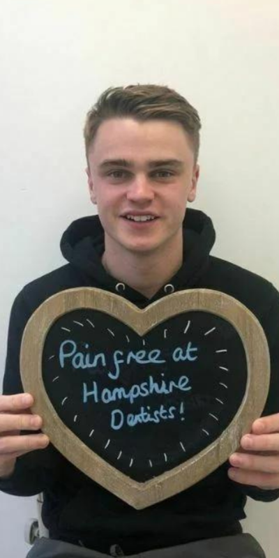 Patient at Hampshire Dentists, holding a sign saying "Pain free at Hampshire Dentists" emphasising pain-free dental care.