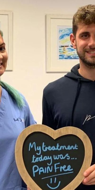 Patient with Dental nurse at Hampshire Dentists, holding a sign saying "My treatment today was pain free" emphasising pain-free dental care.