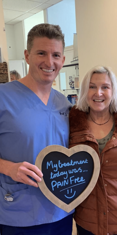 Patient Photos - Hampshire Dentists Pain Free Dentist in Southampton Patient with Dr Robin Hanna at Hampshire Dentists, holding a sign saying "My treatment today was pain free" emphasising pain-free dental care.