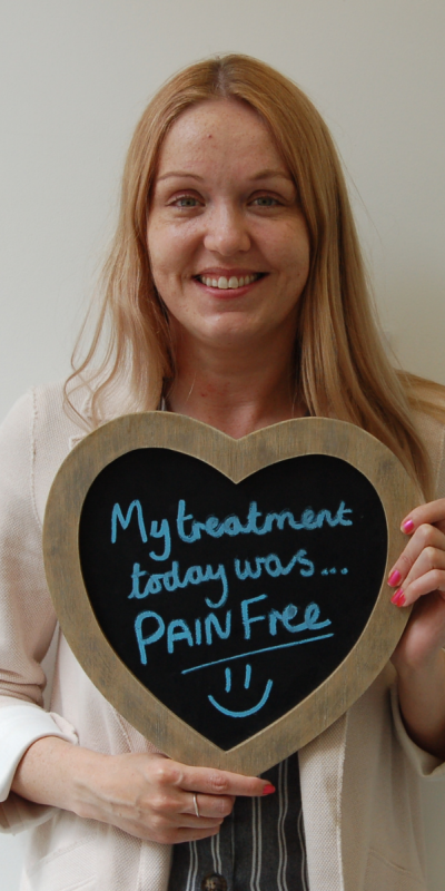 Patient at Hampshire Dentists, holding a sign saying "Pain free at Hampshire Dentists" emphasising pain-free dental care.