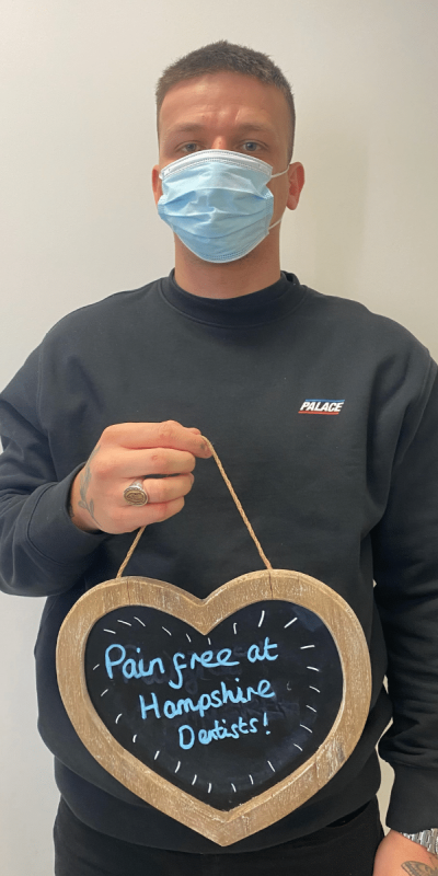 Patient Photos - Hampshire Dentists Pain Free Dentist in Southampton Patient at Hampshire Dentists, holding a sign saying "Pain free at Hampshire Dentists" emphasising pain-free dental care.