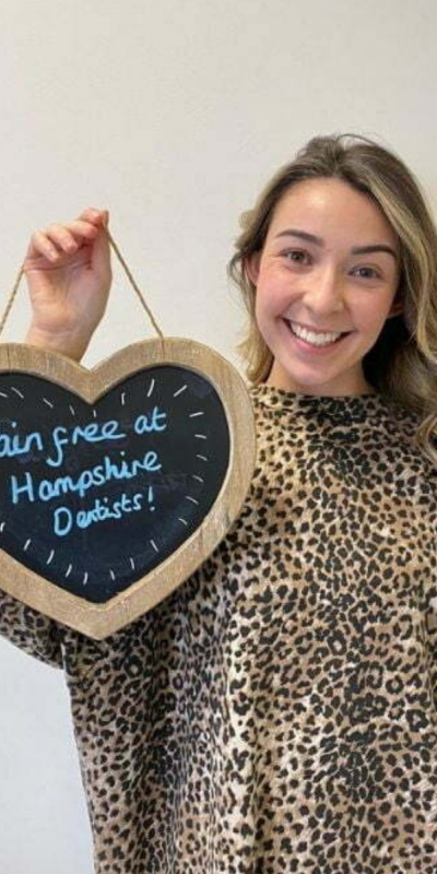 Patient at Hampshire Dentists, holding a sign saying "Pain free at Hampshire Dentists" emphasising pain-free dental care.