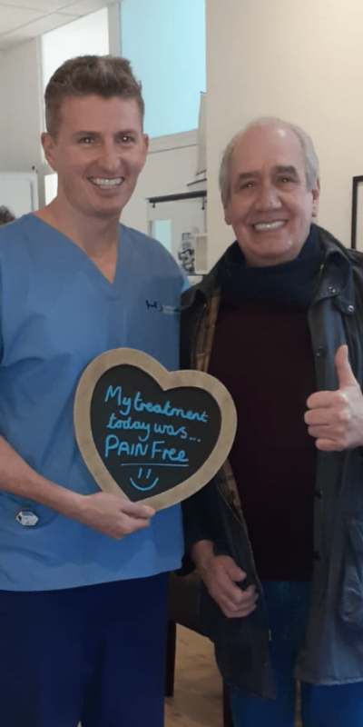 Patient Photos - Hampshire Dentists Pain Free Dentist in Southampton Patient with Dr Robin Hanna at Hampshire Dentists, holding a sign saying "My treatment today was pain free" emphasising pain-free dental care.