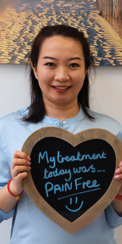 Patient at Hampshire Dentists, holding a sign saying " My treatment today was pain free " emphasising pain-free dental care.