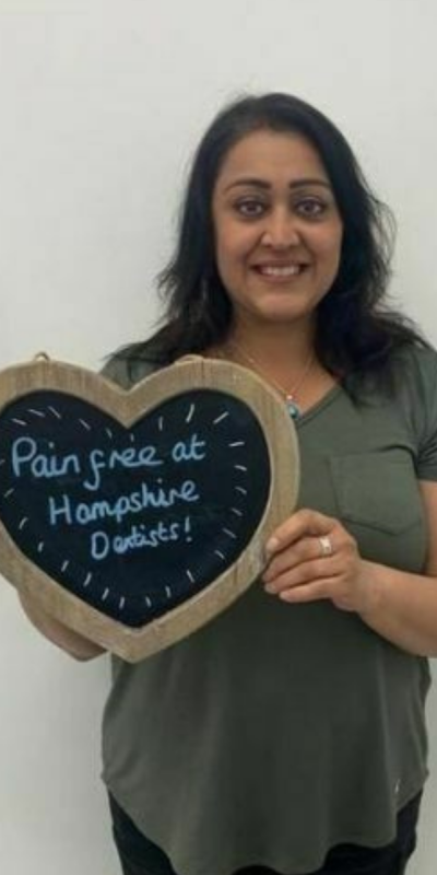 Patient at Hampshire Dentists, holding a sign saying "Pain free at Hampshire Dentists" emphasising pain-free dental care.