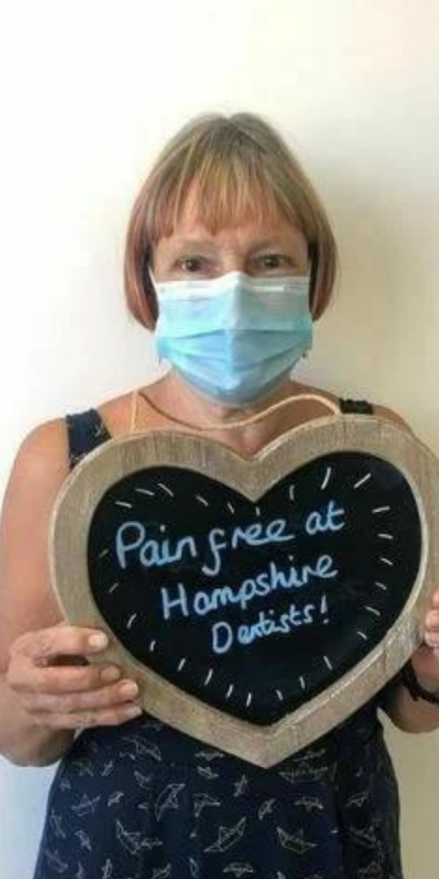 Patient at Hampshire Dentists, holding a sign saying "Pain free at Hampshire Dentists" emphasising pain-free dental care.