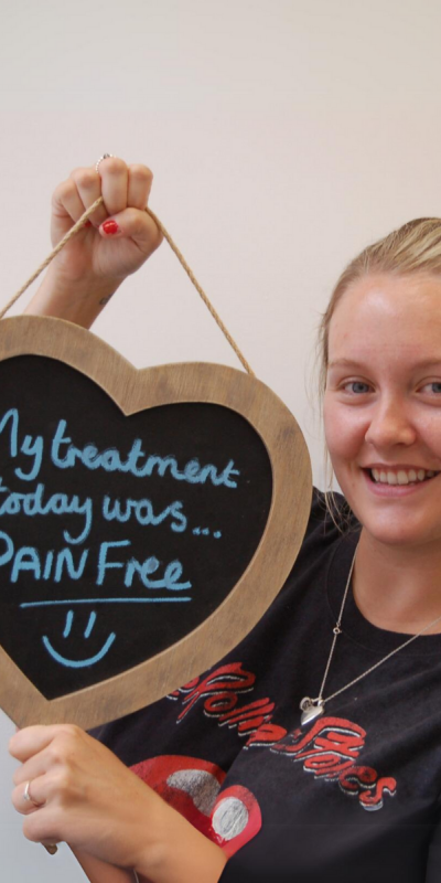 Patient at Hampshire Dentists, holding a sign saying " My treatment today was pain free " emphasising pain-free dental care.