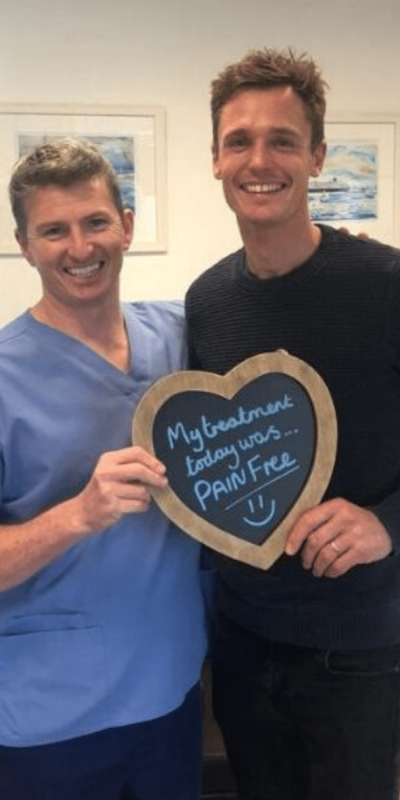 Patient Photos - Hampshire Dentists Pain Free Dentist in Southampton Patient with Dr Robin Hanna at Hampshire Dentists, holding a sign saying "My treatment today was pain free" emphasising pain-free dental care.