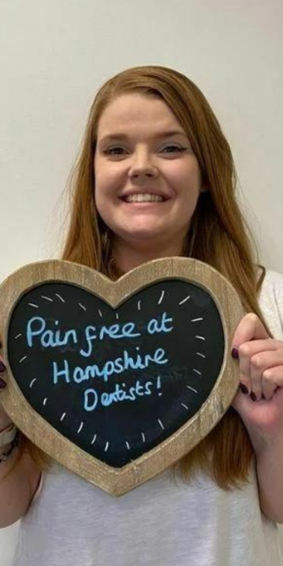 Patient at Hampshire Dentists, holding a sign saying "Pain free at Hampshire Dentists" emphasising pain-free dental care.