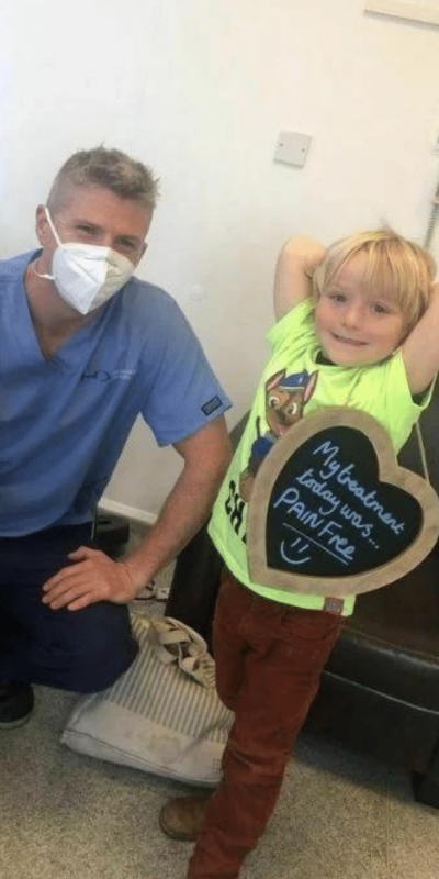 Patient Photos - Hampshire Dentists Pain Free Dentist in Southampton Patient with Dr Robin Hanna at Hampshire Dentists, holding a sign saying "My treatment today was pain free" emphasising pain-free dental care.