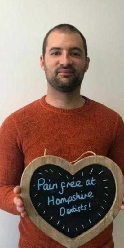 Patient at Hampshire Dentists, holding a sign saying "Pain free at Hampshire Dentists" emphasising pain-free dental care.
