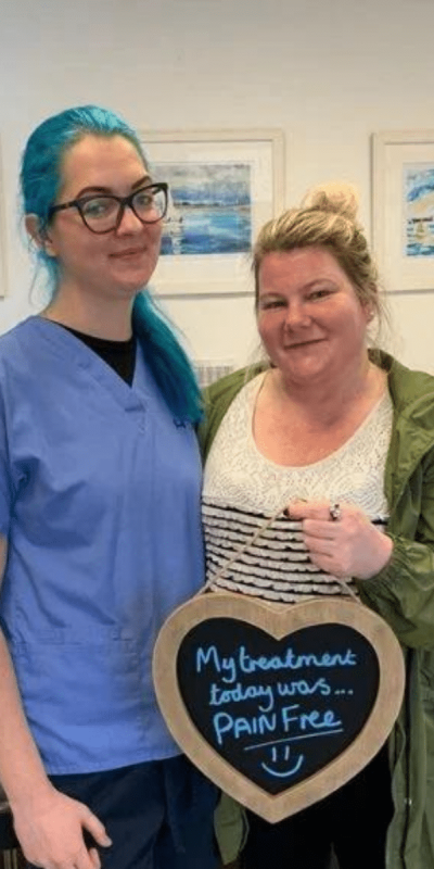 Patient Photos - Hampshire Dentists Pain Free Dentist in Southampton Patient with Dental nurse at Hampshire Dentists, holding a sign saying "My treatment today was pain free" emphasising pain-free dental care.