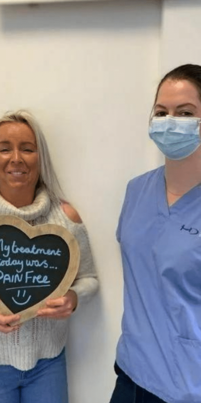 Patient Photos - Hampshire Dentists Pain Free Dentist in Southampton Patient with Dental nurse at Hampshire Dentists, holding a sign saying "My treatment today was pain free" emphasising pain-free dental care.