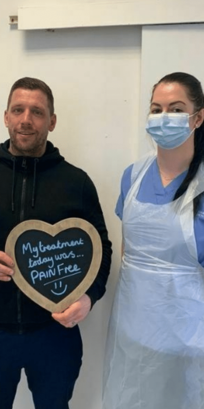 Patient Photos - Hampshire Dentists Pain Free Dentist in Southampton Patient with Dental nurse at Hampshire Dentists, holding a sign saying "My treatment today was pain free" emphasising pain-free dental care.