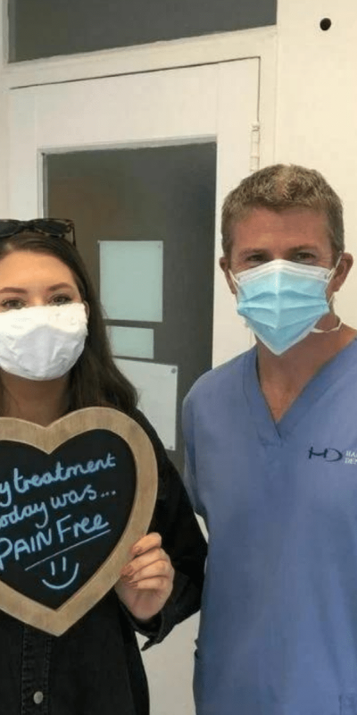 Patient Photos - Hampshire Dentists Pain Free Dentist in Southampton Patient with Dr Robin Hanna at Hampshire Dentists, holding a sign saying "My treatment today was pain free" emphasising pain-free dental care.