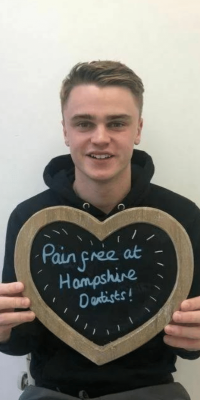 Patient Photos - Hampshire Dentists Pain Free Dentist in Southampton Patient at Hampshire Dentists, holding a sign saying "Pain free at Hampshire Dentists" emphasising pain-free dental care.