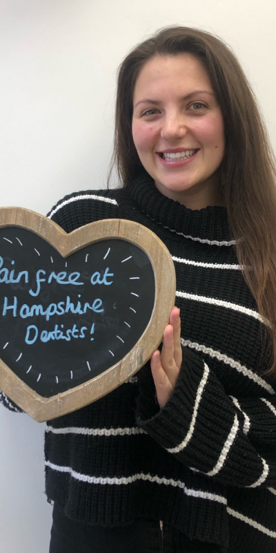 Patient at Hampshire Dentists, holding a sign saying "Pain free at Hampshire Dentists" emphasising pain-free dental care.