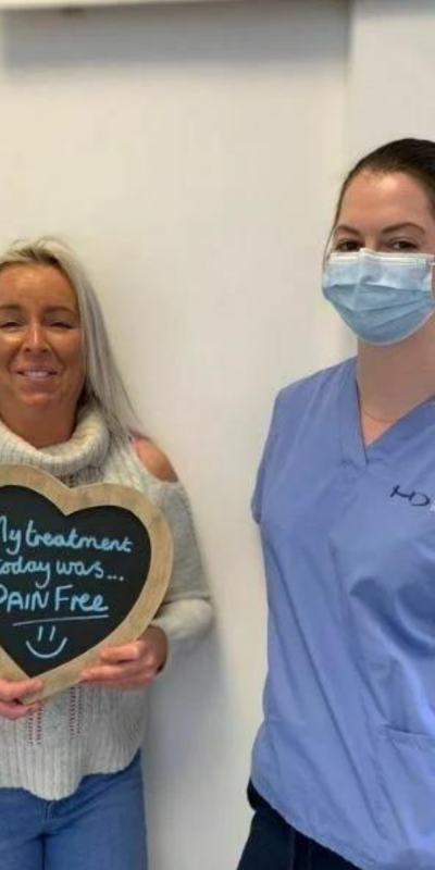 Patient with Dental nurse at Hampshire Dentists, holding a sign saying "My treatment today was pain free" emphasising pain-free dental care.